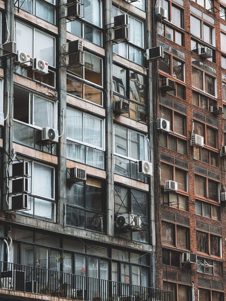 Fachada de predio urbano com varios ar-condicionados nas janelas representando ambientes fechados com ma ventilacao e Sindrome do Edificio Doente