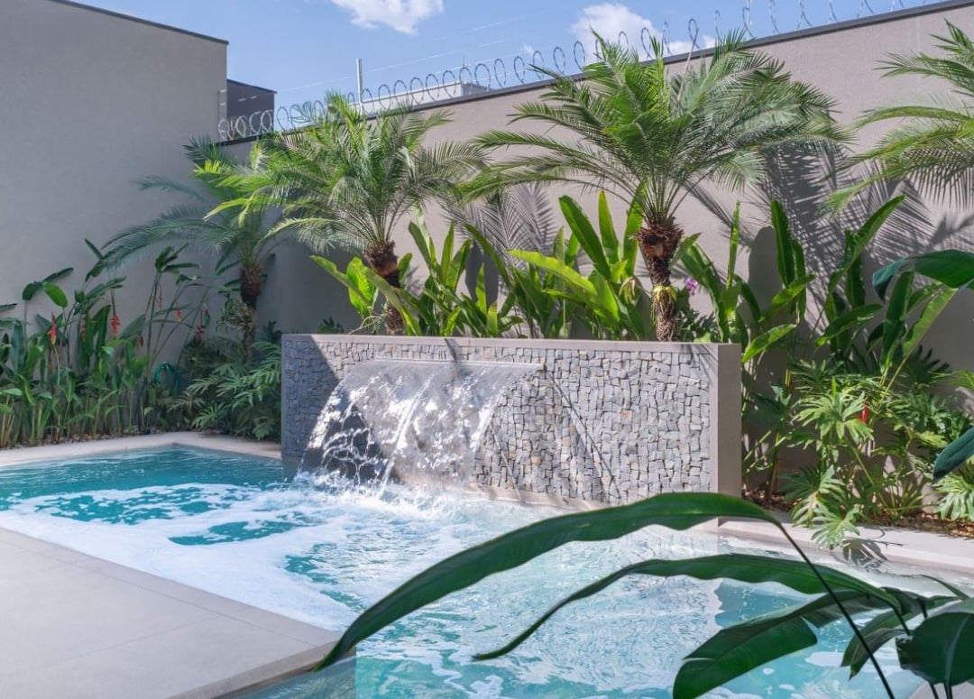 Piscina com cascata de pedra e jardim tropical, resultado de consultoria de paisagismo online bem-sucedida