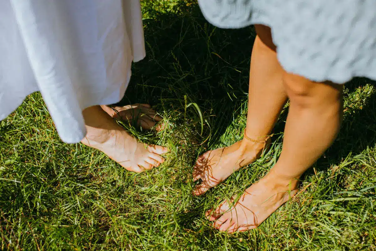 Andar descalço na grama faz bem: pés de duas pessoas pisando em gramado ao sol