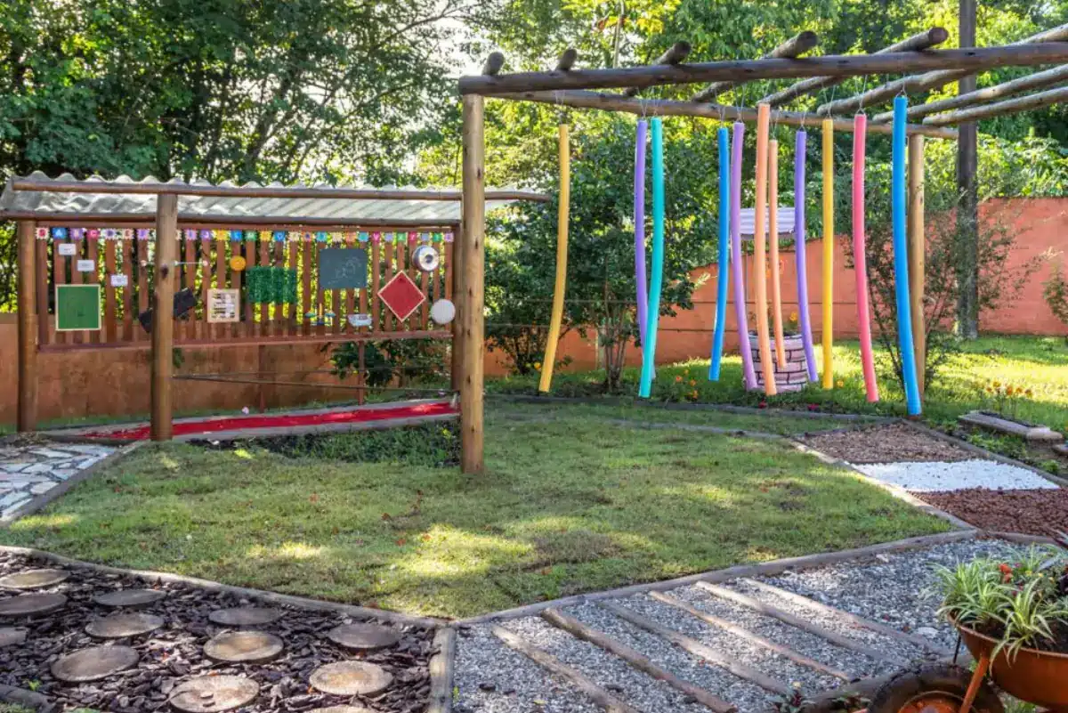 Jardim sensorial infantil com caminho de pedras, gramado e espaguetes de espuma coloridos pendurados